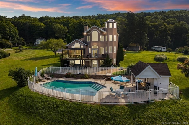 back house at dusk featuring a yard, a fenced in pool, a patio, and a balcony