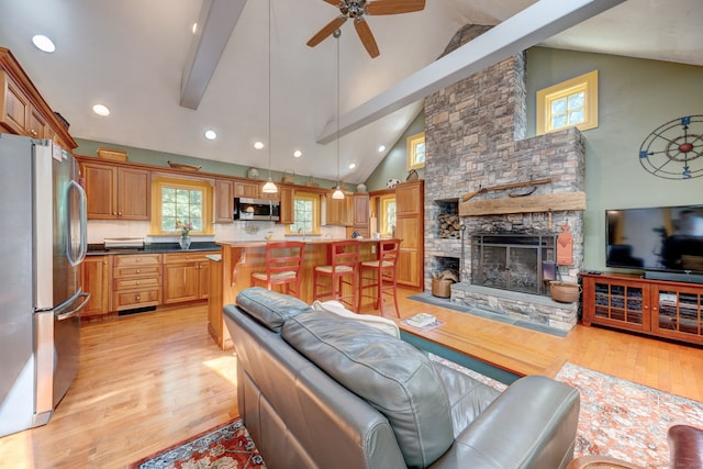 living room with a fireplace, beamed ceiling, light wood-type flooring, and ceiling fan