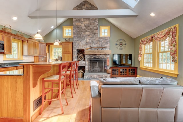 living room featuring sink, a stone fireplace, plenty of natural light, and light hardwood / wood-style flooring