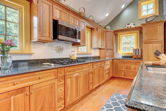 kitchen featuring light hardwood / wood-style flooring, tasteful backsplash, stainless steel appliances, vaulted ceiling, and sink