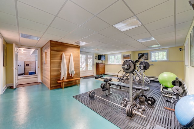 exercise room featuring french doors, wooden walls, and a paneled ceiling