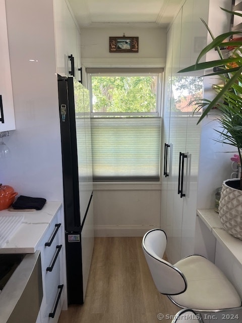 kitchen featuring crown molding, light wood-type flooring, light stone countertops, white cabinets, and black fridge