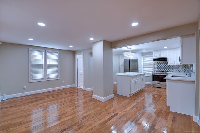 kitchen with appliances with stainless steel finishes, a center island, white cabinetry, and light wood-type flooring