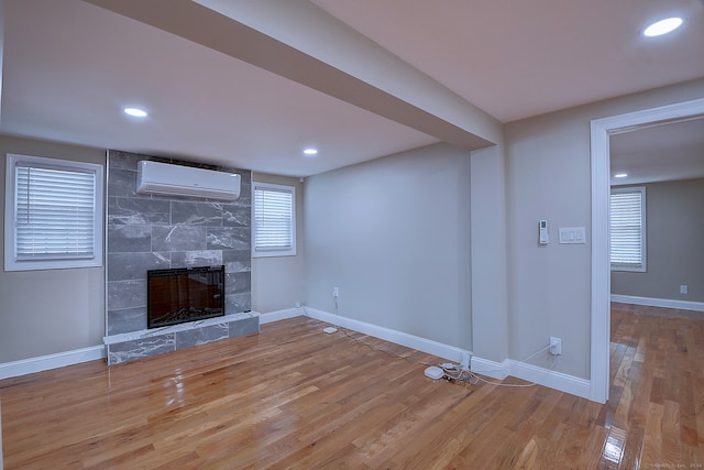 unfurnished living room with tile walls, a wall mounted AC, a tiled fireplace, and wood-type flooring