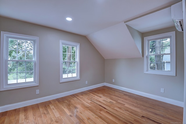 bonus room with light wood-type flooring, plenty of natural light, lofted ceiling, and a wall mounted air conditioner