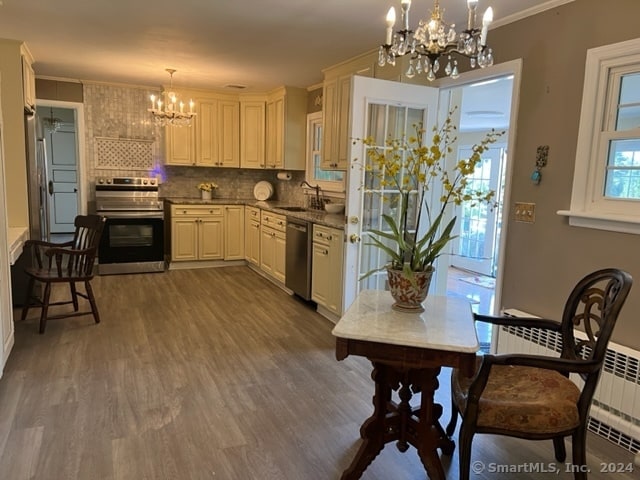 kitchen with an inviting chandelier, appliances with stainless steel finishes, hanging light fixtures, ornamental molding, and hardwood / wood-style flooring