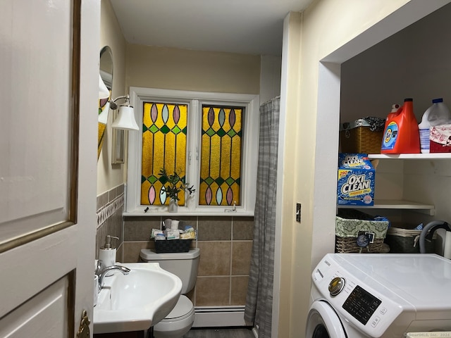 bathroom with a baseboard heating unit, toilet, sink, tile walls, and washer / dryer