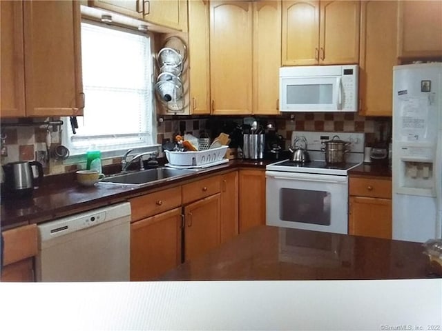 kitchen with backsplash, dark countertops, a sink, and white appliances