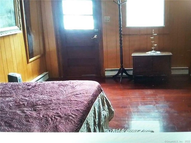 bedroom with wood finished floors, wood walls, and baseboard heating