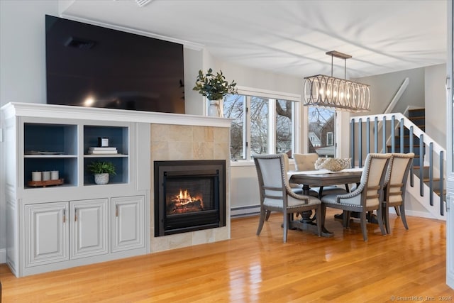 dining area with baseboard heating, a tiled fireplace, hardwood / wood-style flooring, and an inviting chandelier