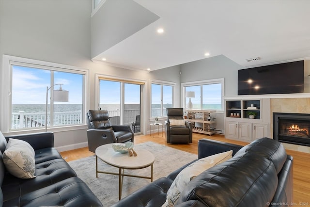 living room with a water view, a tiled fireplace, light hardwood / wood-style flooring, and a baseboard heating unit