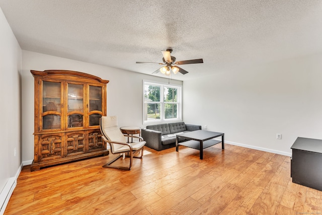 sitting room with ceiling fan, a baseboard heating unit, light hardwood / wood-style flooring, and a textured ceiling