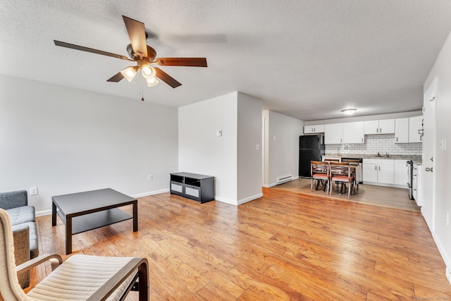 living room with a textured ceiling, ceiling fan, a baseboard heating unit, and light wood-type flooring