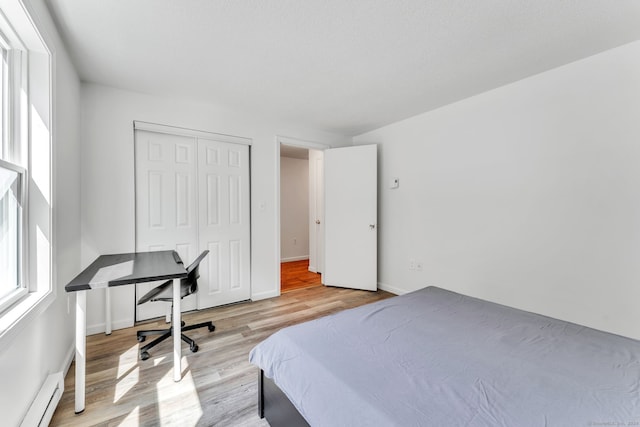 bedroom featuring light hardwood / wood-style flooring, a baseboard heating unit, and a closet