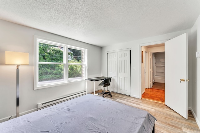 bedroom with light wood-type flooring, a closet, baseboard heating, and a textured ceiling