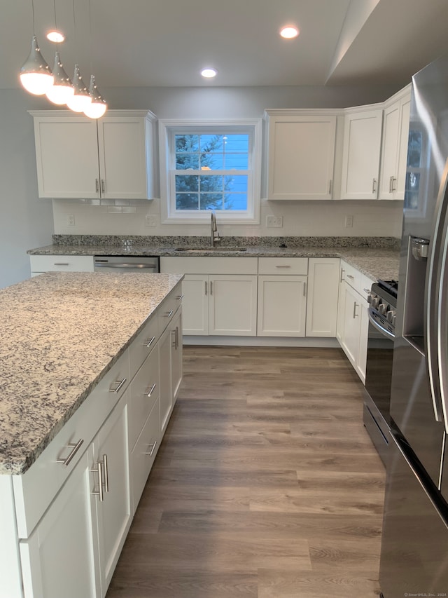 kitchen featuring hardwood / wood-style floors, white cabinetry, light stone countertops, appliances with stainless steel finishes, and sink