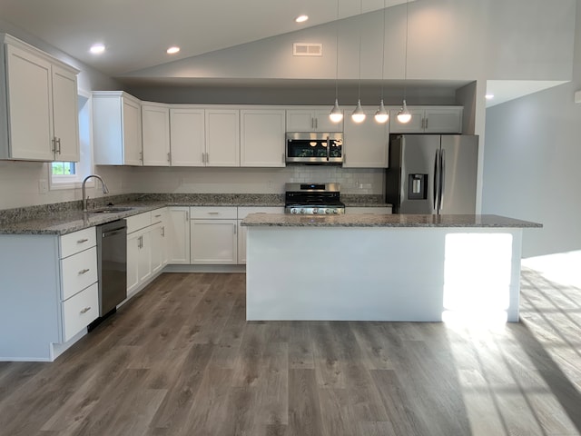 kitchen with vaulted ceiling, sink, stainless steel appliances, and a kitchen island