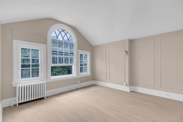 spare room featuring light hardwood / wood-style floors, lofted ceiling, and radiator