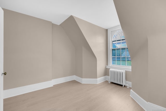 additional living space featuring radiator heating unit, lofted ceiling, and light hardwood / wood-style floors