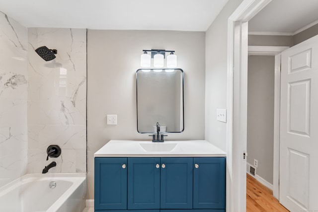 bathroom featuring wood-type flooring, crown molding, tiled shower / bath, and vanity