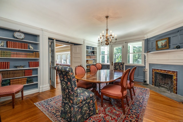 dining space featuring built in shelves, hardwood / wood-style flooring, a notable chandelier, and ornamental molding