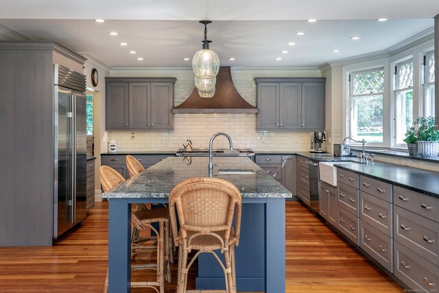 kitchen with custom range hood, dark hardwood / wood-style flooring, an island with sink, a kitchen breakfast bar, and pendant lighting