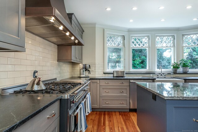 kitchen featuring light hardwood / wood-style flooring, stainless steel appliances, dark stone countertops, and wall chimney range hood