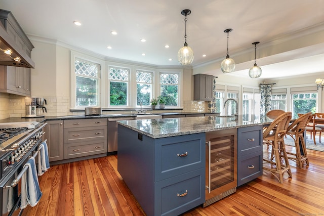 kitchen with wine cooler, a center island with sink, light hardwood / wood-style flooring, stainless steel appliances, and stone counters