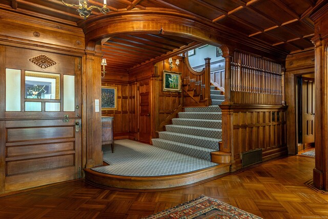 stairway with a notable chandelier, ornate columns, wood walls, and parquet floors