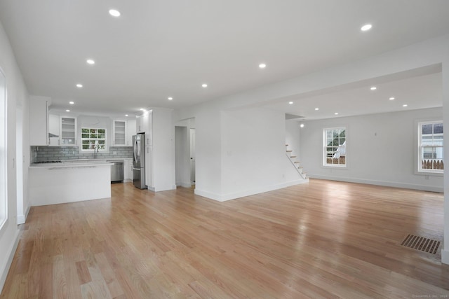 unfurnished living room with stairs, light wood-style flooring, plenty of natural light, and visible vents