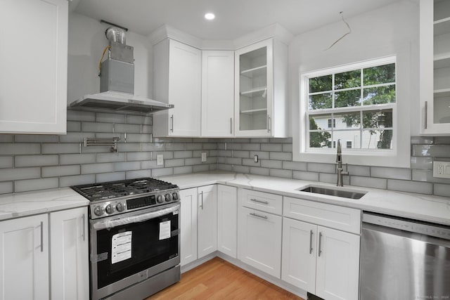 kitchen with tasteful backsplash, white cabinets, stainless steel appliances, wall chimney range hood, and a sink