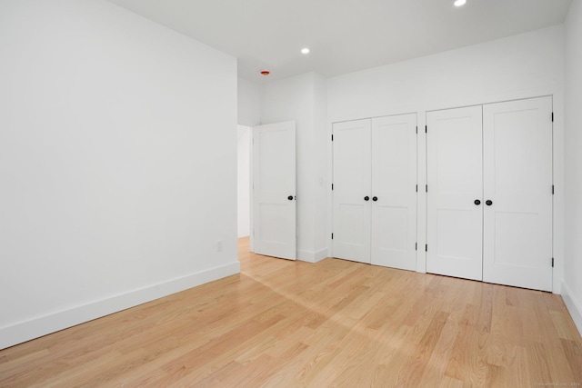 unfurnished bedroom featuring recessed lighting, wood finished floors, baseboards, and two closets