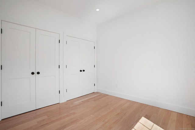 unfurnished bedroom featuring light wood-style floors, recessed lighting, baseboards, and multiple closets