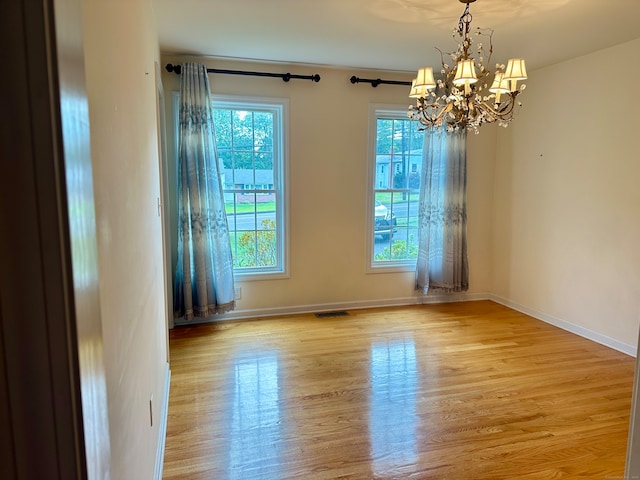 spare room with light wood-type flooring and a chandelier