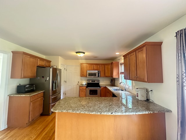 kitchen featuring light hardwood / wood-style floors, kitchen peninsula, sink, light stone countertops, and appliances with stainless steel finishes