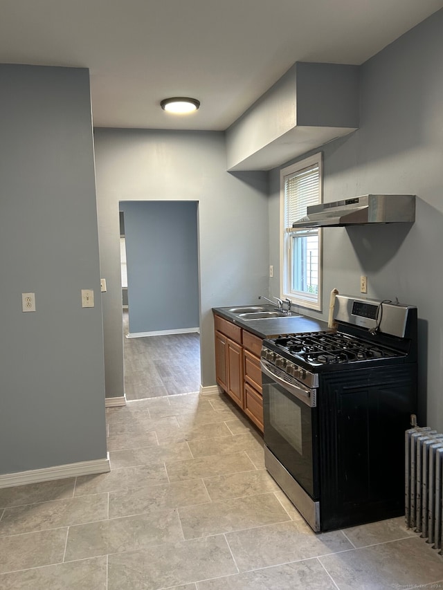 kitchen featuring radiator heating unit, gas range, sink, and wall chimney range hood