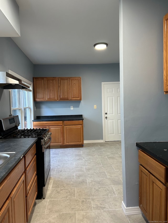 kitchen featuring stainless steel gas stove, dark stone countertops, and wall chimney range hood