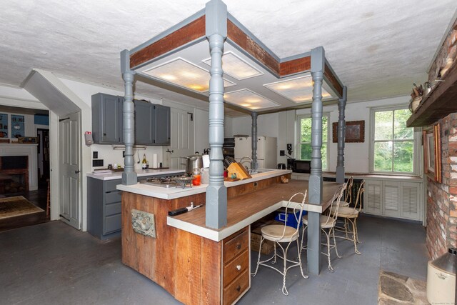 kitchen featuring concrete floors, brick wall, white refrigerator, and gray cabinetry