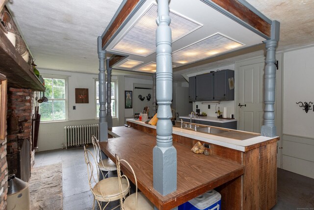 kitchen featuring radiator heating unit, brick wall, gray cabinetry, sink, and light tile patterned flooring