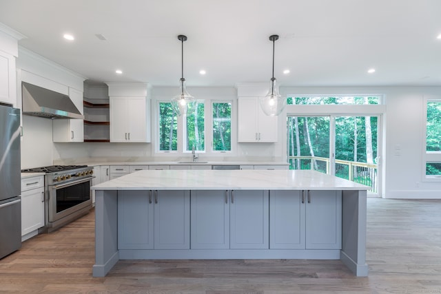 kitchen featuring pendant lighting, light hardwood / wood-style flooring, a center island, appliances with stainless steel finishes, and wall chimney range hood