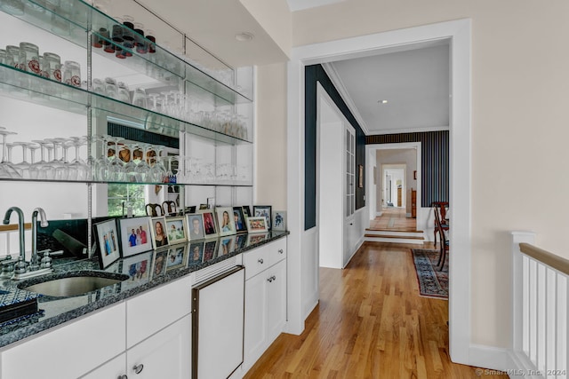 bar featuring white cabinets, light wood-type flooring, ornamental molding, dark stone countertops, and sink