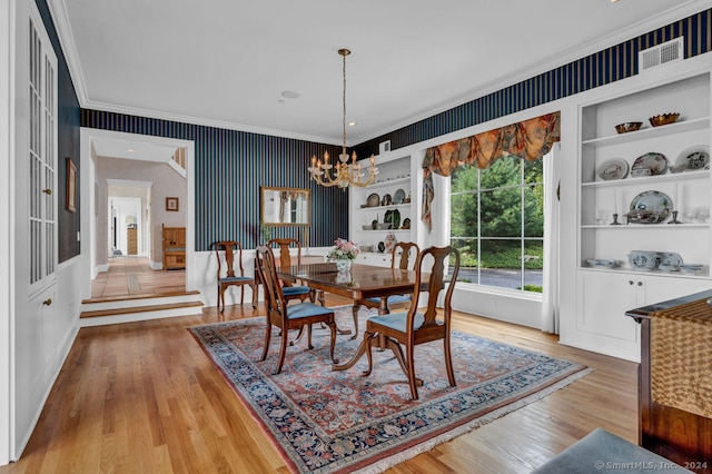 dining area with ornamental molding, built in features, a notable chandelier, and light hardwood / wood-style floors