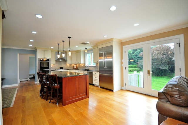 kitchen with stainless steel appliances, crown molding, french doors, wall chimney range hood, and a sink