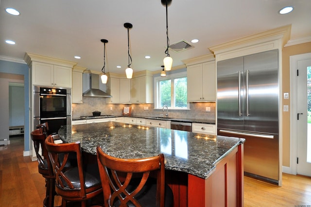 kitchen with light wood-style flooring, a sink, ornamental molding, appliances with stainless steel finishes, and wall chimney exhaust hood