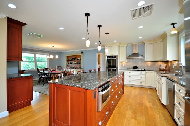 kitchen with visible vents, wall chimney exhaust hood, appliances with stainless steel finishes, crown molding, and a sink