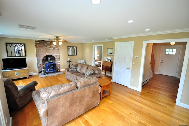 living area featuring visible vents, a wood stove, baseboard heating, crown molding, and light wood-style floors