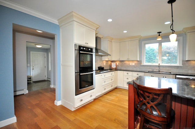 kitchen featuring stainless steel appliances, a sink, ornamental molding, light wood-type flooring, and wall chimney exhaust hood