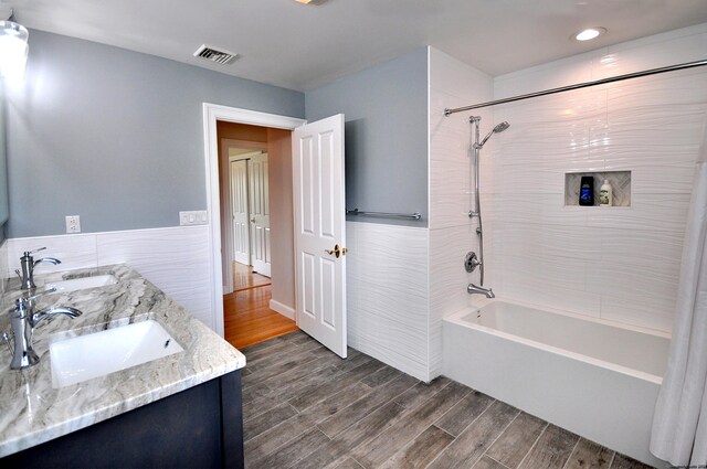 full bathroom featuring wood finished floors, a sink, visible vents, shower / bathing tub combination, and double vanity