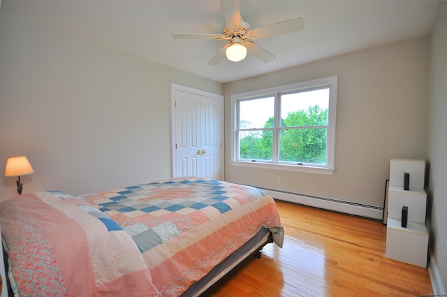 bedroom with a baseboard heating unit, a closet, ceiling fan, and light wood finished floors