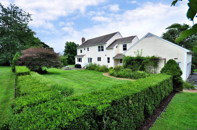 rear view of house with an attached garage, a chimney, and a yard